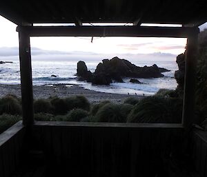 A sunrise over a small bay is framed by the verandah of the hut