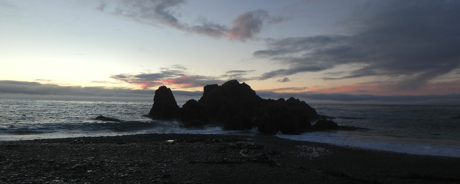 A pink sunrise over a rocky outcrop and horizon