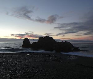 A pink sunrise over a rocky outcrop and horizon