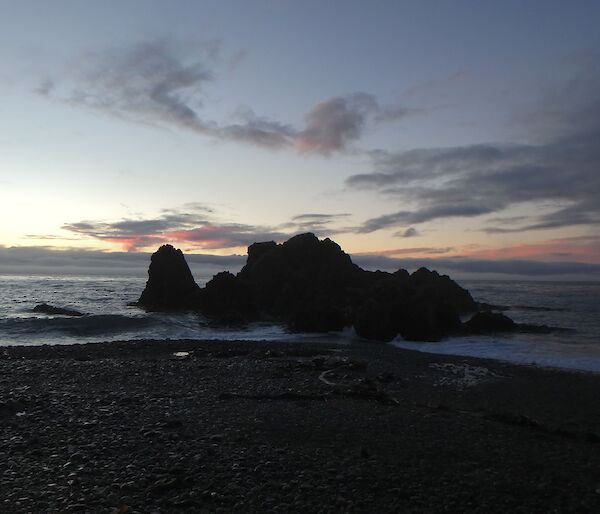 A pink sunrise over a rocky outcrop and horizon