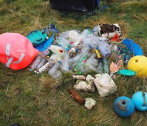 a stack of colourful plastic debris is piled up on the grass including plastic bottles and buoys
