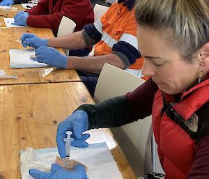 Three people wearing blue gloves are practising injecting a needle into a piece of flesh