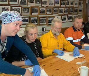 four people wearing blue gloves are practising how to use needles for injections