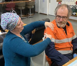 a doctor is demonstrating an injection technique on the arm of a man wearing an orange shirt