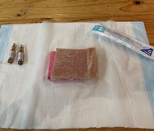 Some expired medication, pork flesh and syringe needle are on a surgical mat