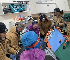 A group of people hold a slide a dummy from a stretcher to a bed