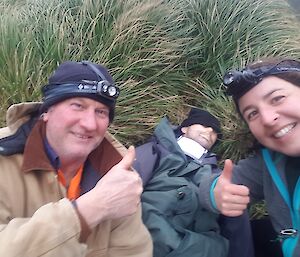 a man and a woman give a thumbs up in front of a dummy laying on the grass