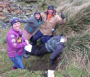 three people stand around a dummy laying in the tussock