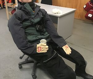 A life sized male dummy sits in a chair holding a cup