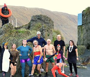 Nine people in various fancy dress stand in front of a rock near an elephant seal, a woman stands on the rock with a life ring around her neck