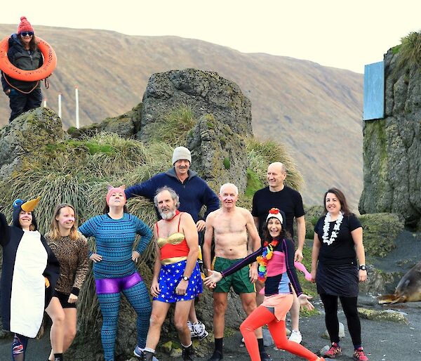 Nine people in various fancy dress stand in front of a rock near an elephant seal, a woman stands on the rock with a life ring around her neck