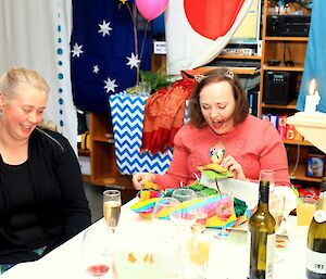 A woman is very happy to open a gift as another woman watches her