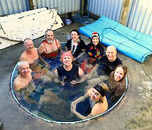 nine people sit in a circle in an outdoor spa bath