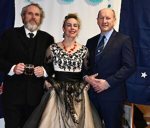 A woman in a black and white dress stands between two men in suits