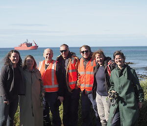 7 people stand on the foreshore with the red Aurora Australis in the background.