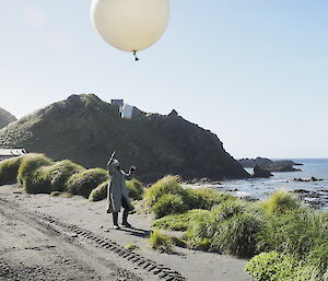 Person wearing grey jacket releasing observation balloon in the sunshine