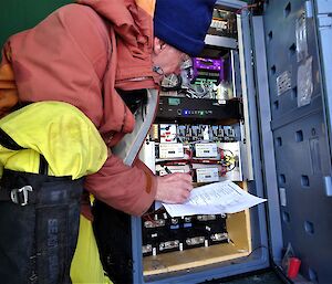 A man crouches next to a computer server housed in a small hut