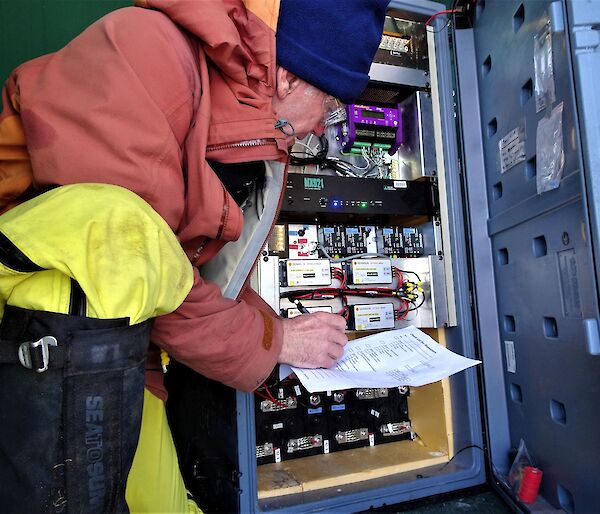 A man crouches next to a computer server housed in a small hut