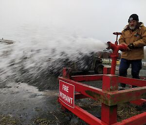 a mand stands in front of a red fire hydrant with water spurting out of it