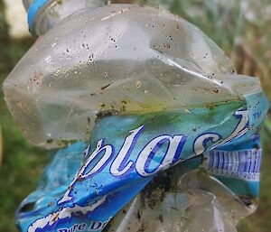 A crumpled clear plastic water bottle with label still attached