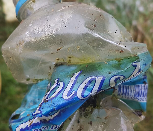 A crumpled clear plastic water bottle with label still attached