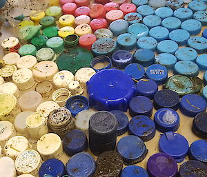 An array of coloured plastic lids are spread out grouped in blues, pinks and whites