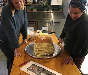 Two women have a layered cake in front of them and are looking at photos of elephant seals