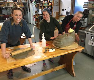 Three women are standing around a cake rolling and shaping dough into an elephant seal head