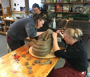 Three women crouch around a cake in the shape of an elephant seal