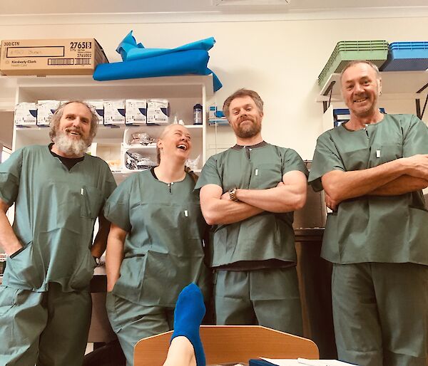 Three men and one woman stand in a line dressed in green hospital scrubs