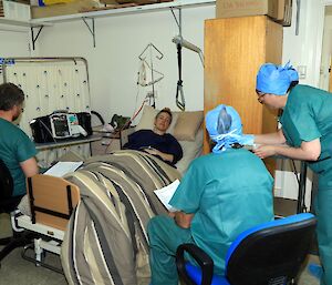 Three people in scrubs stand around a patient laying in a hospital bed