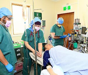 A patient lays in a hospital bed surrounded by three people in scrubs and face masks