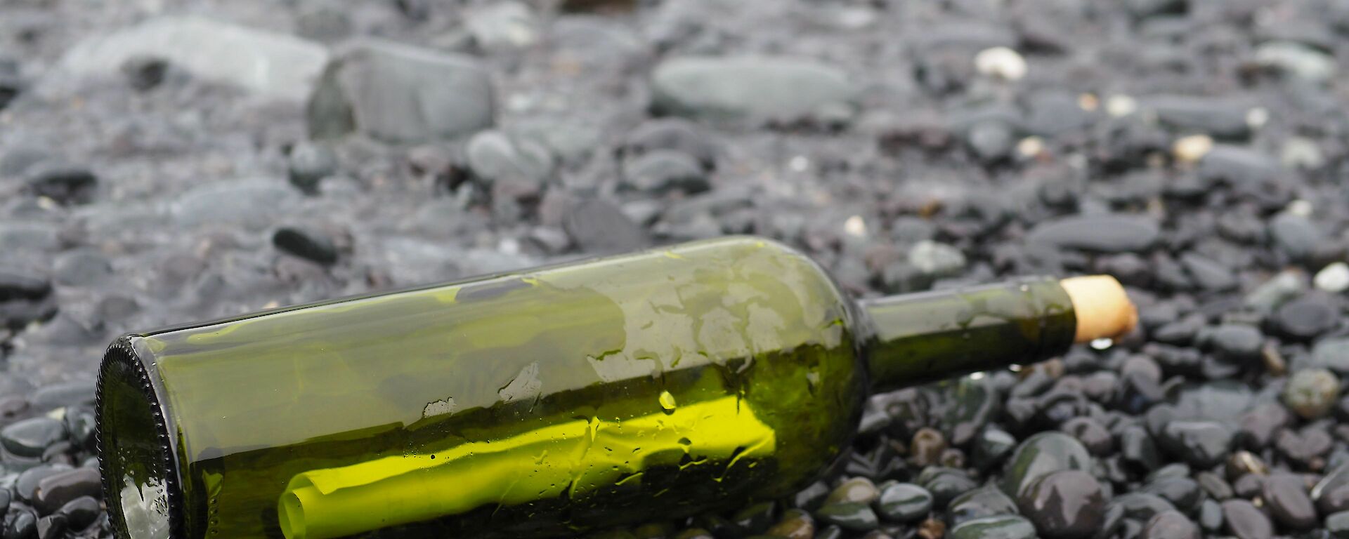 A green bottle lays on a black pebble beach