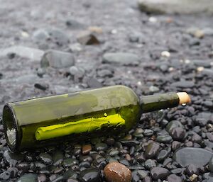 A green bottle lays on a black pebble beach