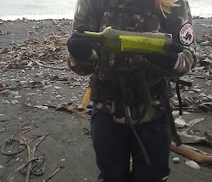 A woman wearing a cap holds a green bottle on a beach