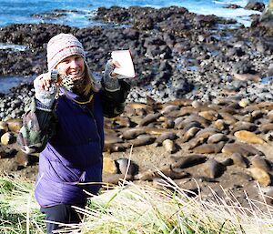 A woman stands on the side of a cliff holding a counter and notebook