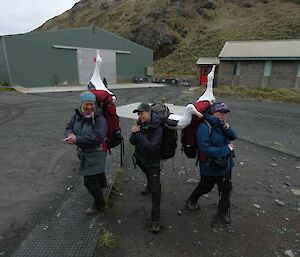 Three women stand together carrying backpacks with fibre glass albatross’