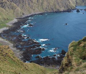 two people walk up a steep tussock cliff overlooking a bay