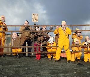 a line up of people in yellow jump suits with face masks stand in front of a gate