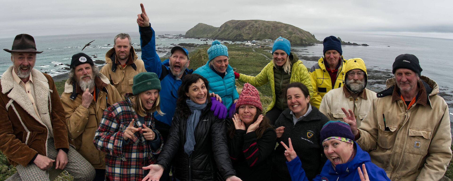 A colourful team of seven men and seven women stand at a look out with an island in the background