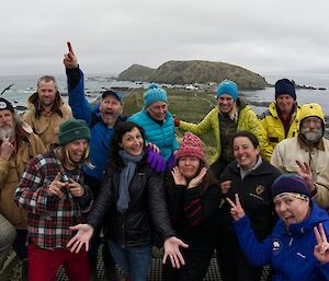 A colourful team of seven men and seven women stand at a look out with an island in the background