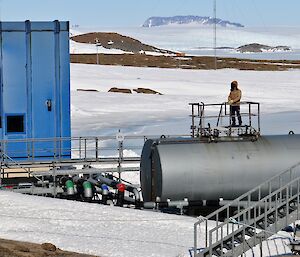 Man stands on large fuel tank with sea ice and plateau in background