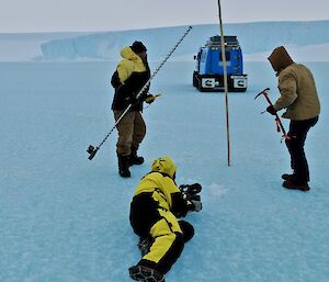 Camerman lying on sea ice to film two people with drill