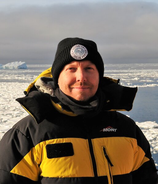 Captain Paul Clarke on the deck of the Aurora Australis with sea ice behind.