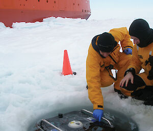 Two people deploy a remotely operated vehicle into an ice hole beside the Aurora Australis.