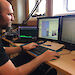 Dr Brian Miller listens for whales during a voyage, with a computer screen in front of him showing sounds.