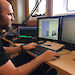 Dr Brian Miller listens for whales during a voyage, with a computer screen in front of him showing sounds.