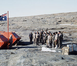 men stand to attention in front of flag on rocky coast