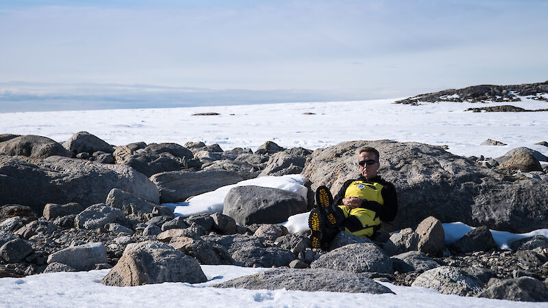 A man sitting against rocks and snow in Antarctica.