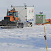 A tractor towing a shipping container on a sled across the Antarctic ice sheet.